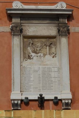 Chiesa dei Santi Apostoli, lapide commemorativa Edicola con decorazione a volute nell'estremità superiore. All'interno lapide con altorilievo rappresentante il compianto di una donna sulla tomba del caro morto in guerra, e iscrizione con i nomi dei caduti durante la Grande Guerra. La lapide è delimitata ai lati da paraste e capitelli decorati.