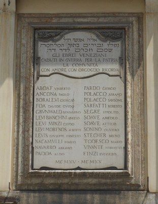  Lapide sorretta da un'ampia cornice sagomata a listelli degradanti. Gli angoli superiori sono decorati da motivi floreali; sotto, una lastra di marmo di Pietra Santa riporta le formule dedicatorie ebraiche. A seguire, dedica commemorativa in italiano con i nomi degli ebrei caduti durante il Primo Conflitto Mondiale.