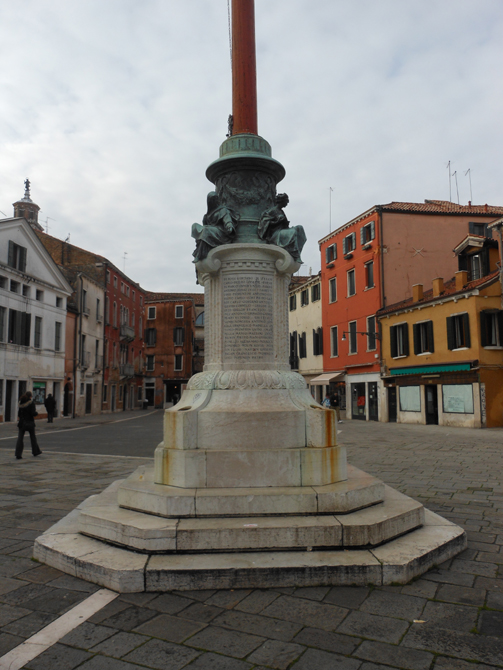 Pilo monumentale portabandiera posto su tre gradini ottagonali. Nel blocco inferiore, su due lati curvilinei, sono riportati i nomi dei caduti della seconda guerra mondiale. Sopra una stretta cornice con modanatura ad ovolo &egrave; il corpo centrale dell'opera, costituito da un pilastro a base curvilinea, che sul fusto mostra iscrizioni commemorative dei caduti della prima guerra mondiale. Lo sormonta un capitello a volute decorato da un motivo a dentelli, sul quale poggia un gruppo bronzeo raffigurante personificazioni di virt&ugrave; assise. All'estremit&agrave; del pennone &egrave; il leone marciano con spada sguainata.