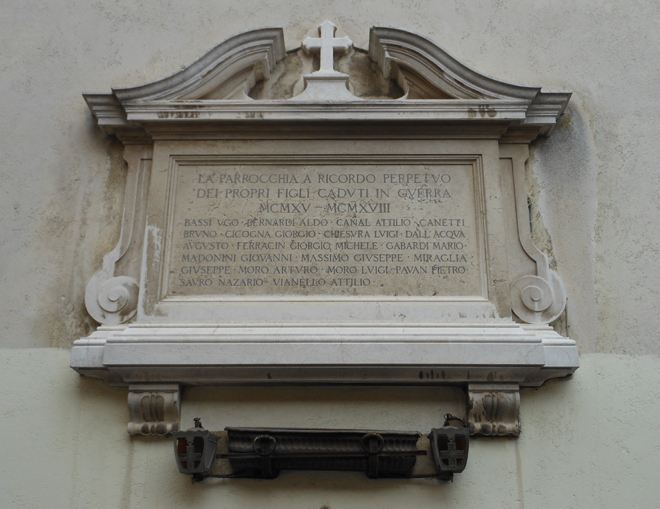 Chiesa di Santa Maria del Giglio, lapide commemorativa Edicola con cornice modanata e timpano curvilineo interrotto, al cui centro è una croce latina dalle estremità patenti. Al centro, sulla lastra è inciso l'elenco dei nomi dei caduti della Prima Guerra Mondiale. Sotto l'opera è collocato un vaso rettangolare in bronzo affiancato da due lanterne votive.